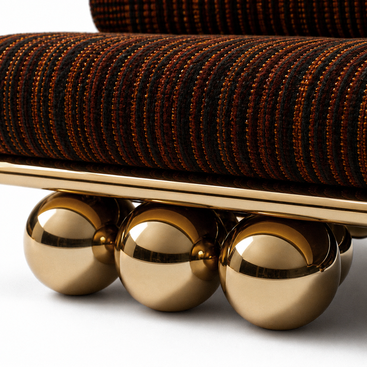 Close-up of the Lustra Sofa showing rich textured fabric, warm copper-gold threads, polished gold rail, and mirror-like sphere legs.