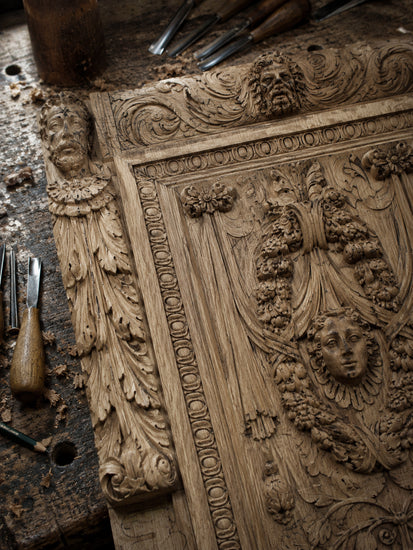 Close-up of black hand-carved wooden cabinet details with sculptural faces and floral ornament.