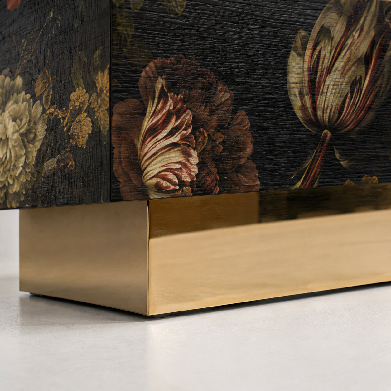 Close-up of the Aurelia sideboard’s polished brass plinth, dark oak veneer and richly detailed botanical façade.