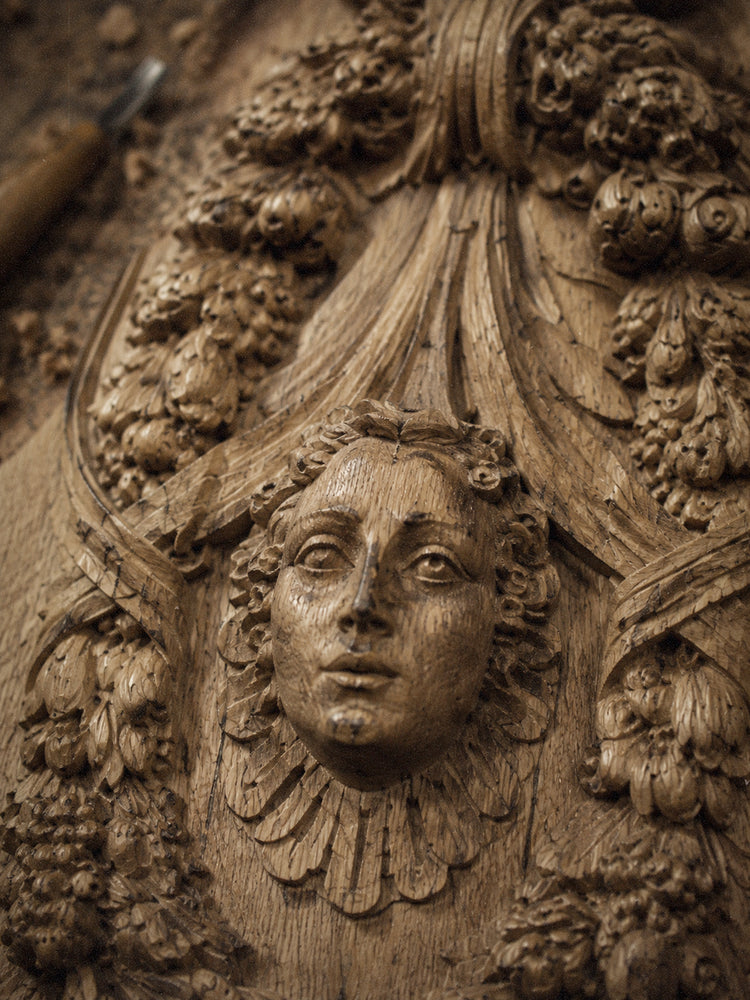Close-up of black hand-carved wooden cabinet details with sculptural faces and floral ornament.