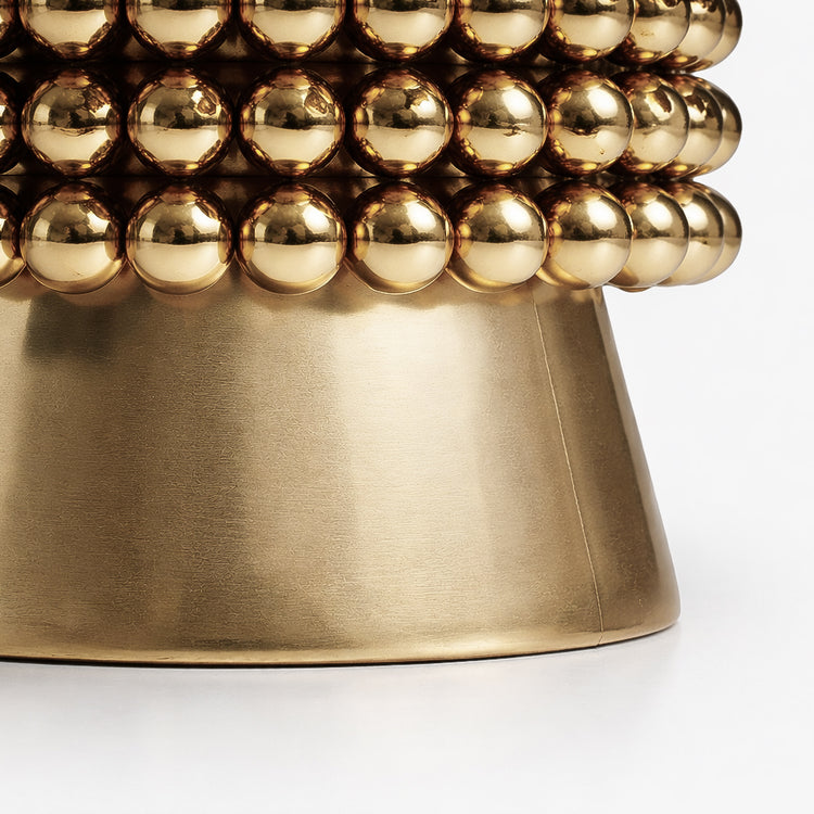 Macro detail of the Lustra table base featuring stacked gold-plated spheres above a brushed brass pedestal with subtle texture.