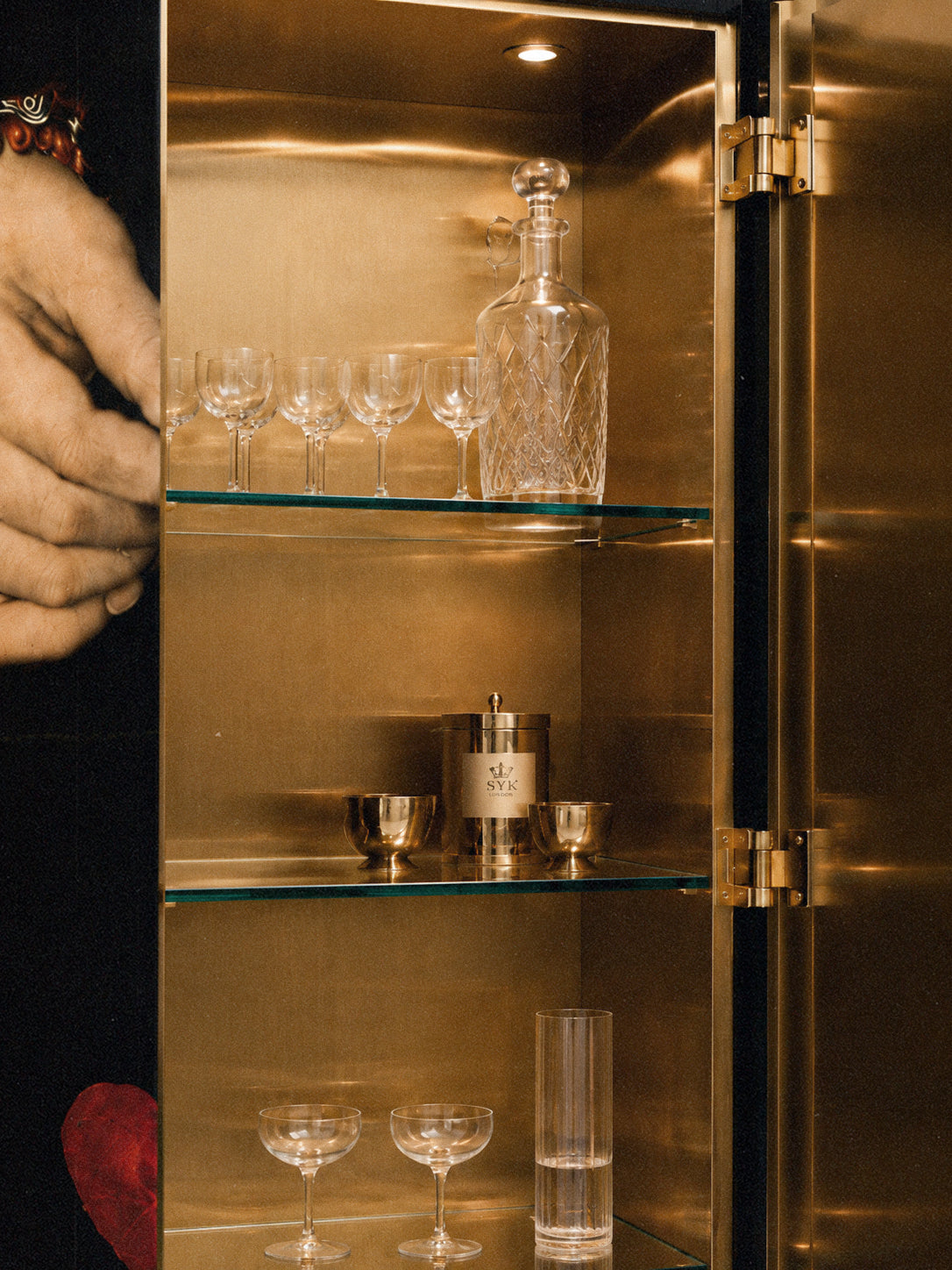 Open Amora cabinet showing illuminated brass panels, glassware, bottles and refined bar storage.