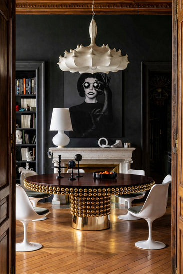 Lustra round dining table by Hekla Property styled in an elegant interior with parquet flooring, sculptural white chairs, fireplace backdrop, and statement artwork.