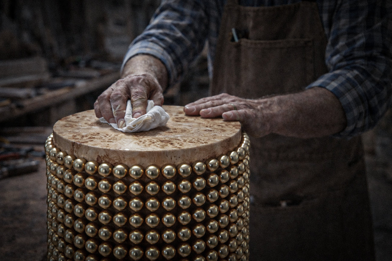 Person cleaning a round wooden object with gold studs using a cloth.