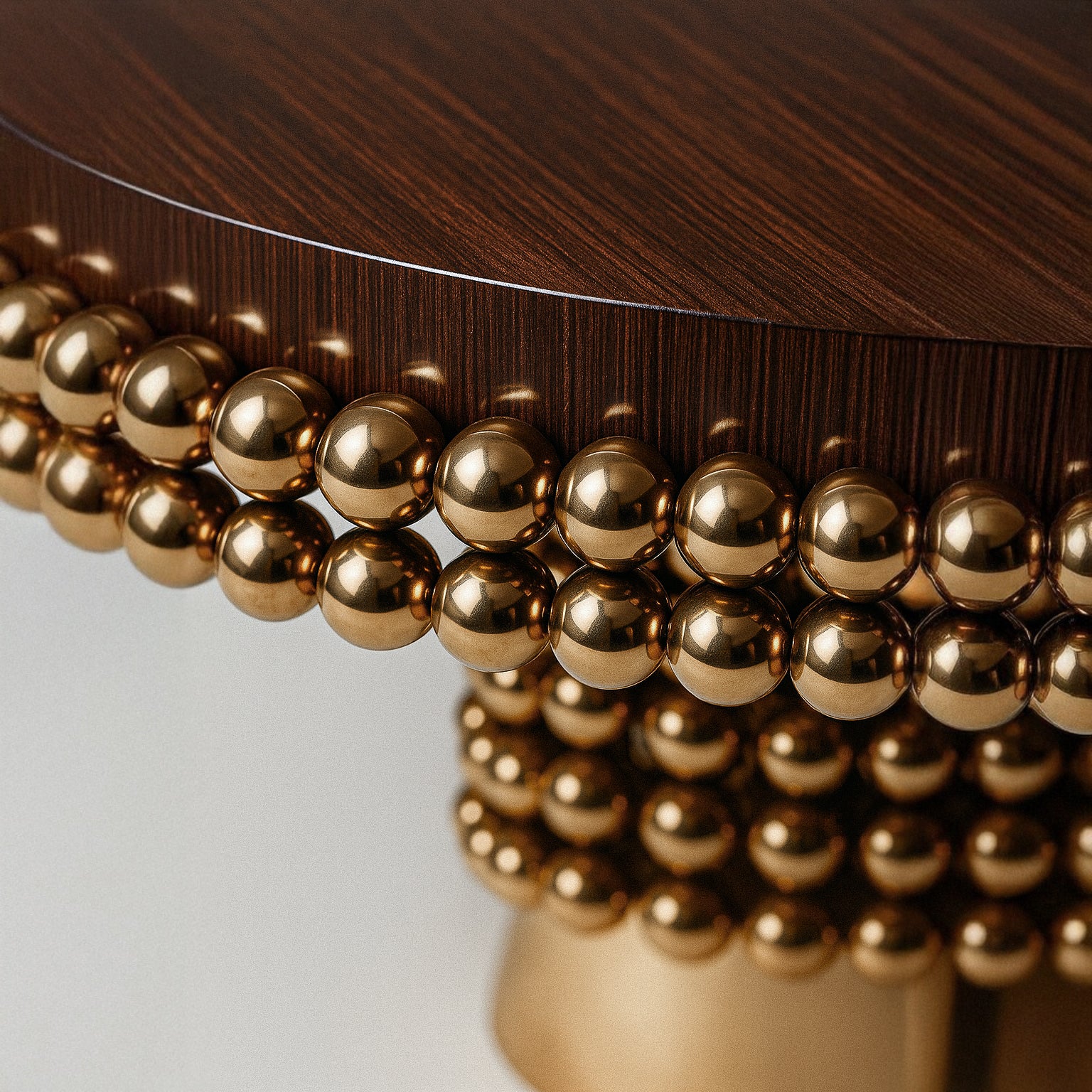 Side profile of the Lustra dining table showcasing layered polished gold spheres and a cylindrical brass pedestal base beneath a rich dark wood tabletop.