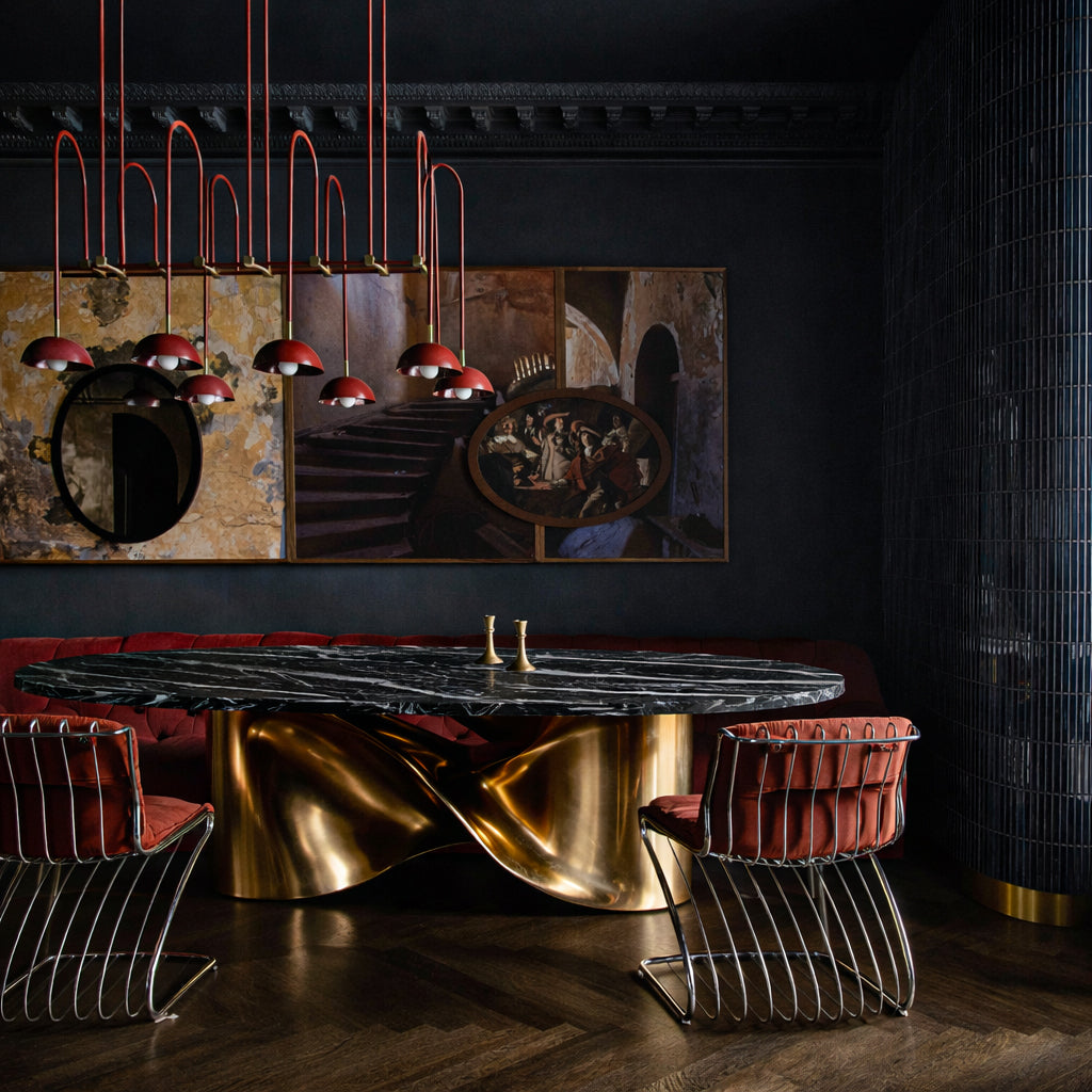 Radiance oval dining table styled with brass candlesticks and design books in moody interior.