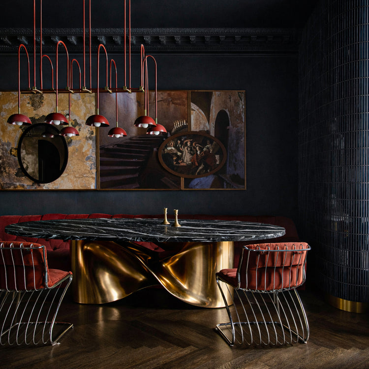 Radiance oval dining table styled with brass candlesticks and design books in moody interior.
