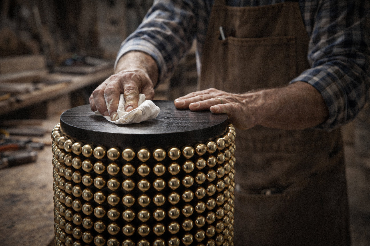 Person cleaning a wooden stool with gold studs in a workshop setting