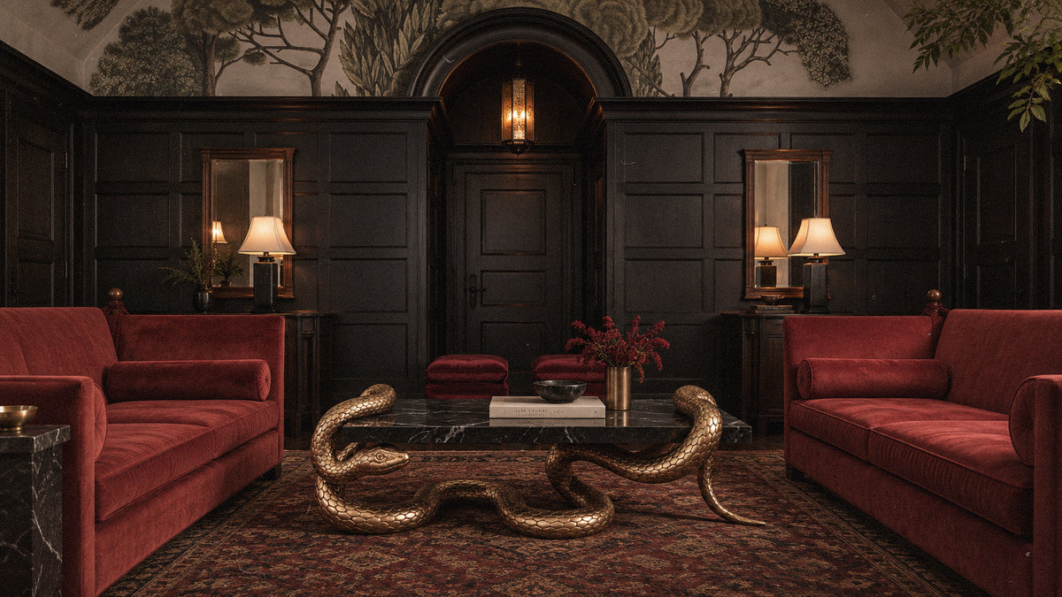 A luxurious dark wood-paneled room with two plush red velvet sofas facing a black marble coffee table with a sculptural gold snake base, set on a patterned rug.